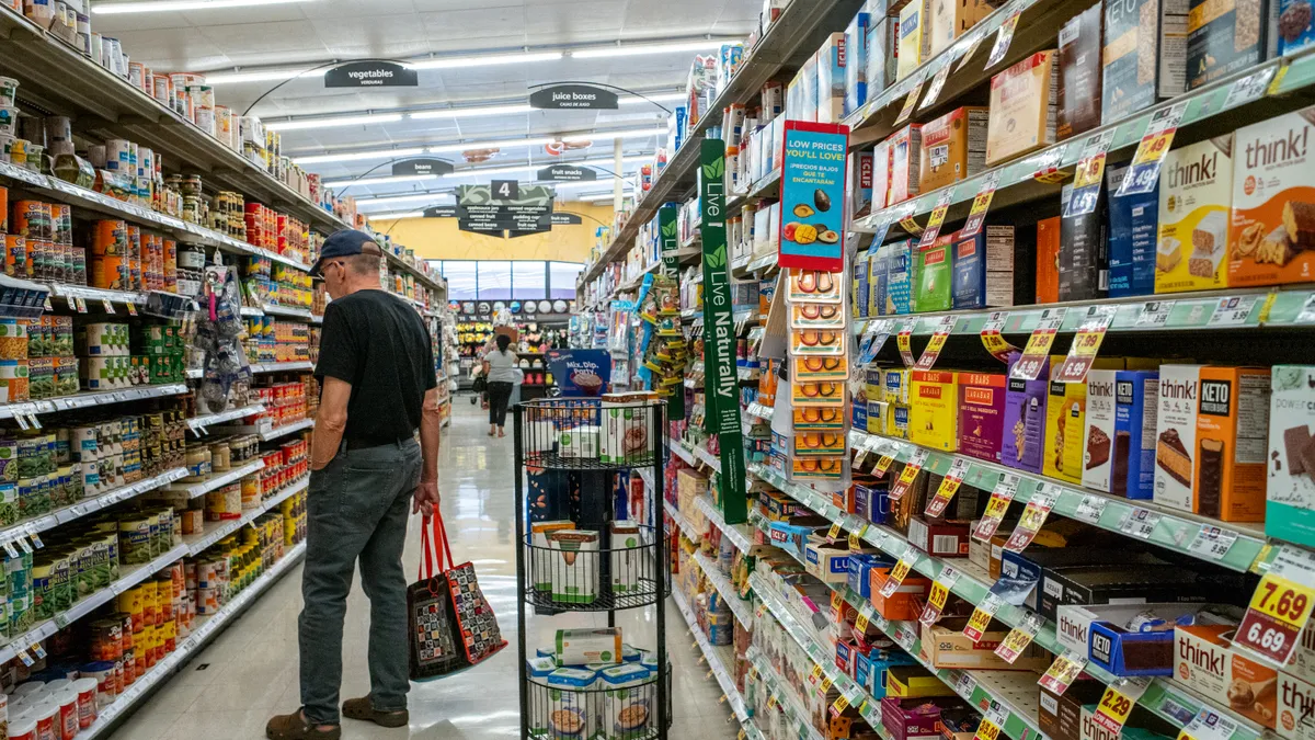 A person carrying a tote bag looks at items on a grocery store shelf